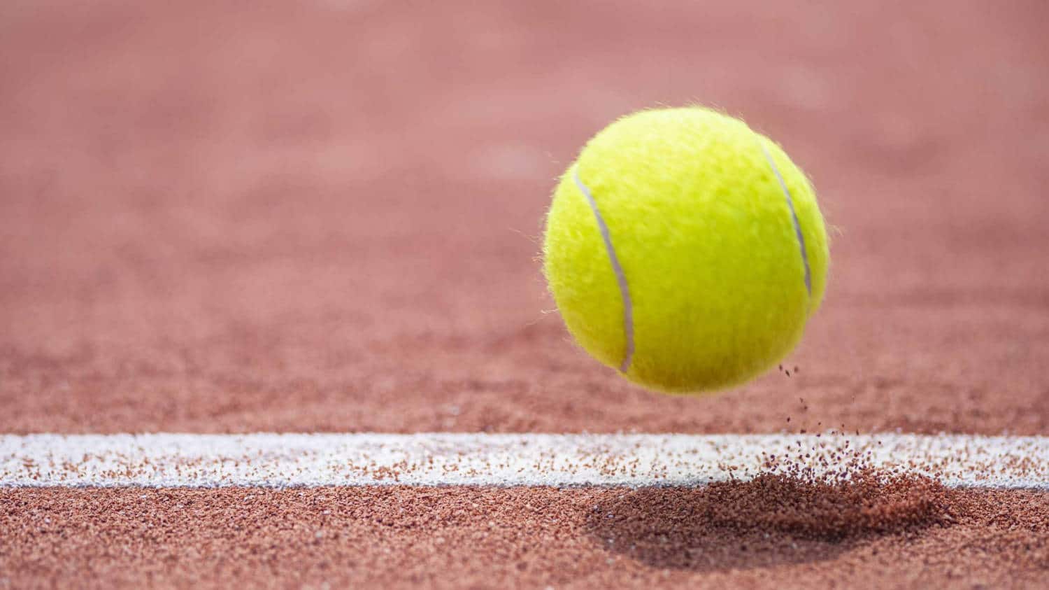 Tennisball springt ab auf weißer Linie. Sandplatz.